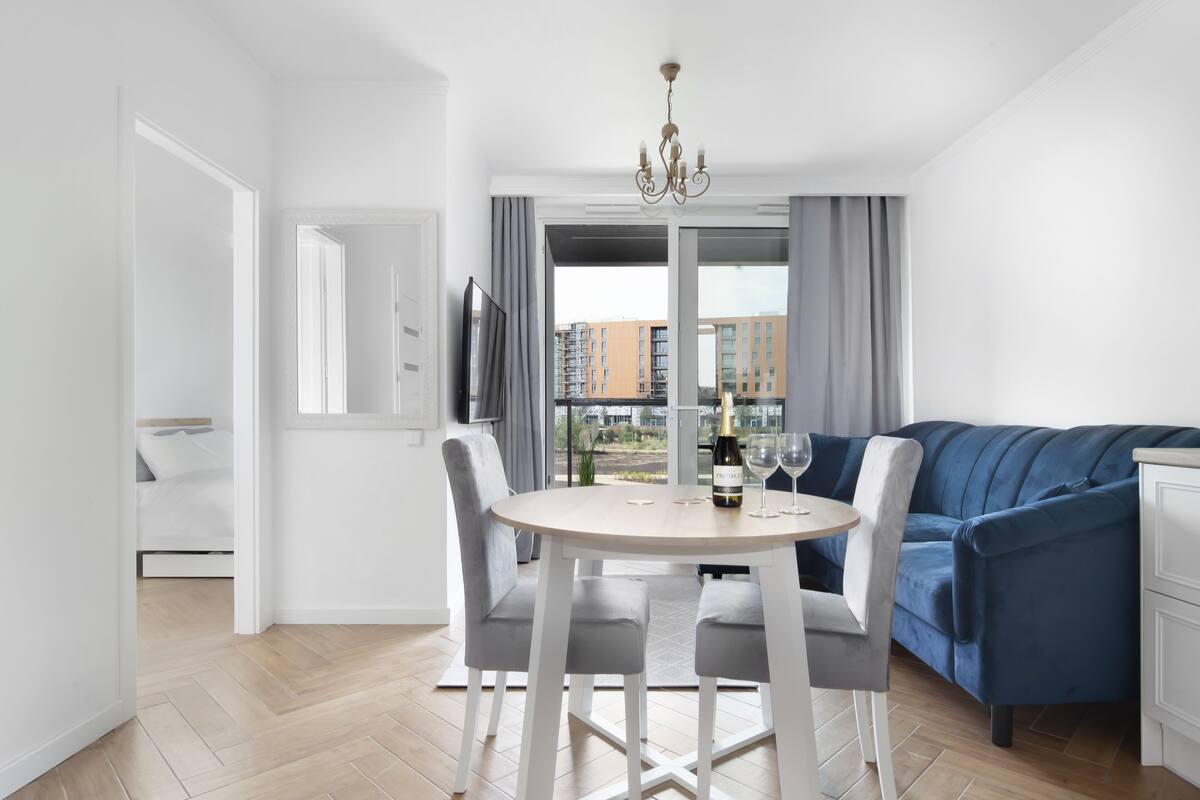 Una sala de estar moderna con un sofá azul, una mesa de comedor con sillas y una araña.