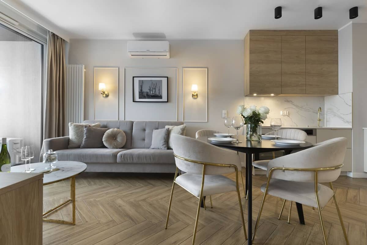 Una sala de estar moderna con sofá, mesa de comedor y sillas, una cocina con armarios de madera e iluminación empotrada.