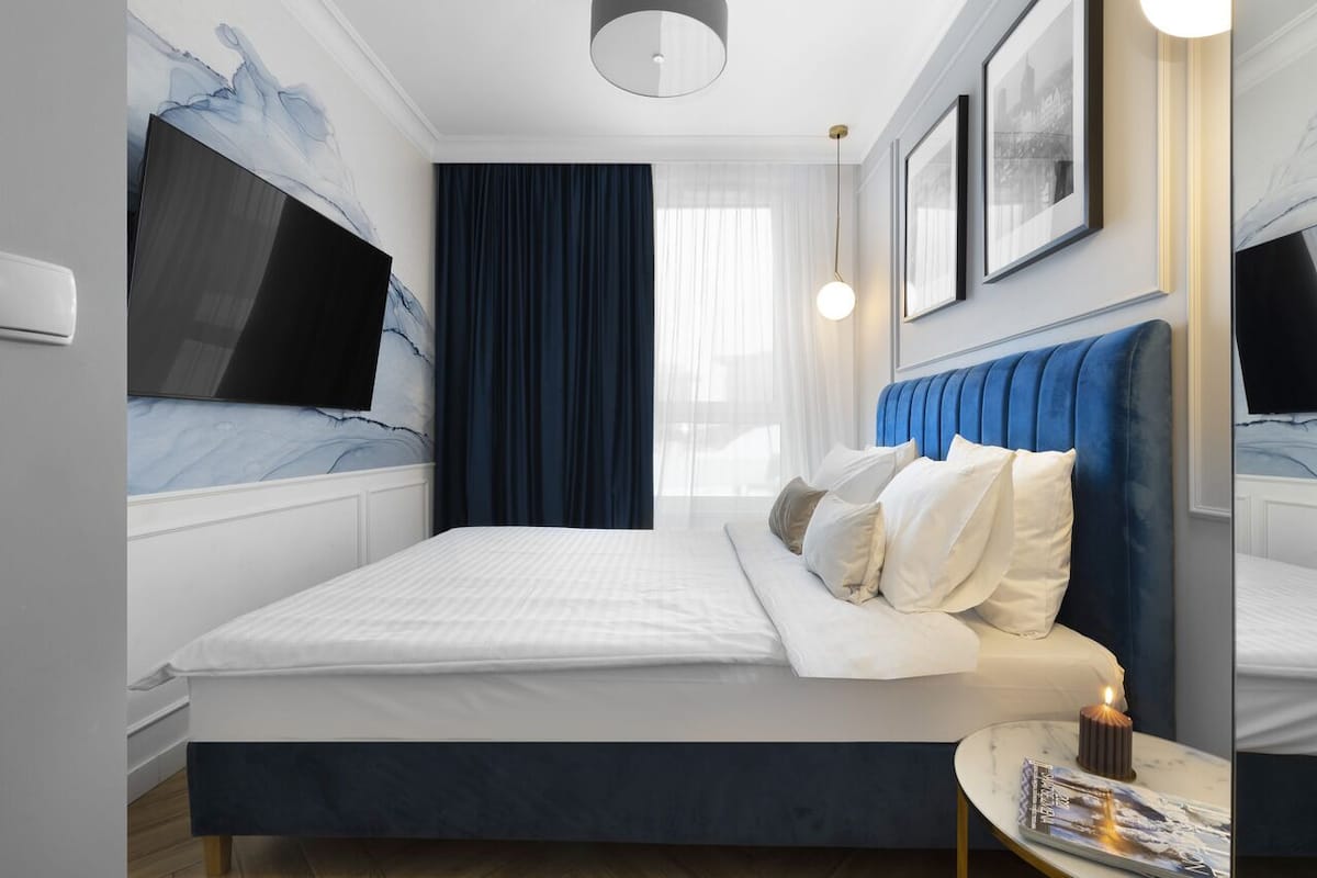 Una habitación de hotel moderna con una cama grande, un televisor de pantalla plana y una mesita de noche con una revista.