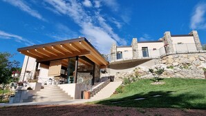 Una casa moderna con fachada de piedra, una pérgola de madera y una escalera de piedra que conduce a la entrada.