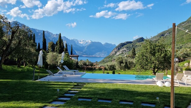Un área de piscina con sillones de descanso, un edificio pequeño y vistas a montañas y un lago.