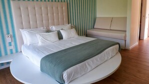 Un dormitorio moderno con cabecera capitonada, cama redonda, sofá y pared a rayas.