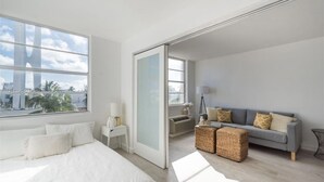 Una habitación de hotel moderna con una cama grande, un sofá, una mesita y vistas de la ciudad a través de amplios ventanales.