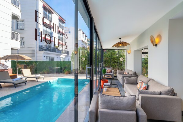 A modern hotel room with a glass wall overlooking a swimming pool, a sofa, and a dining area. - Echinus Lara Hotel (Antalya)