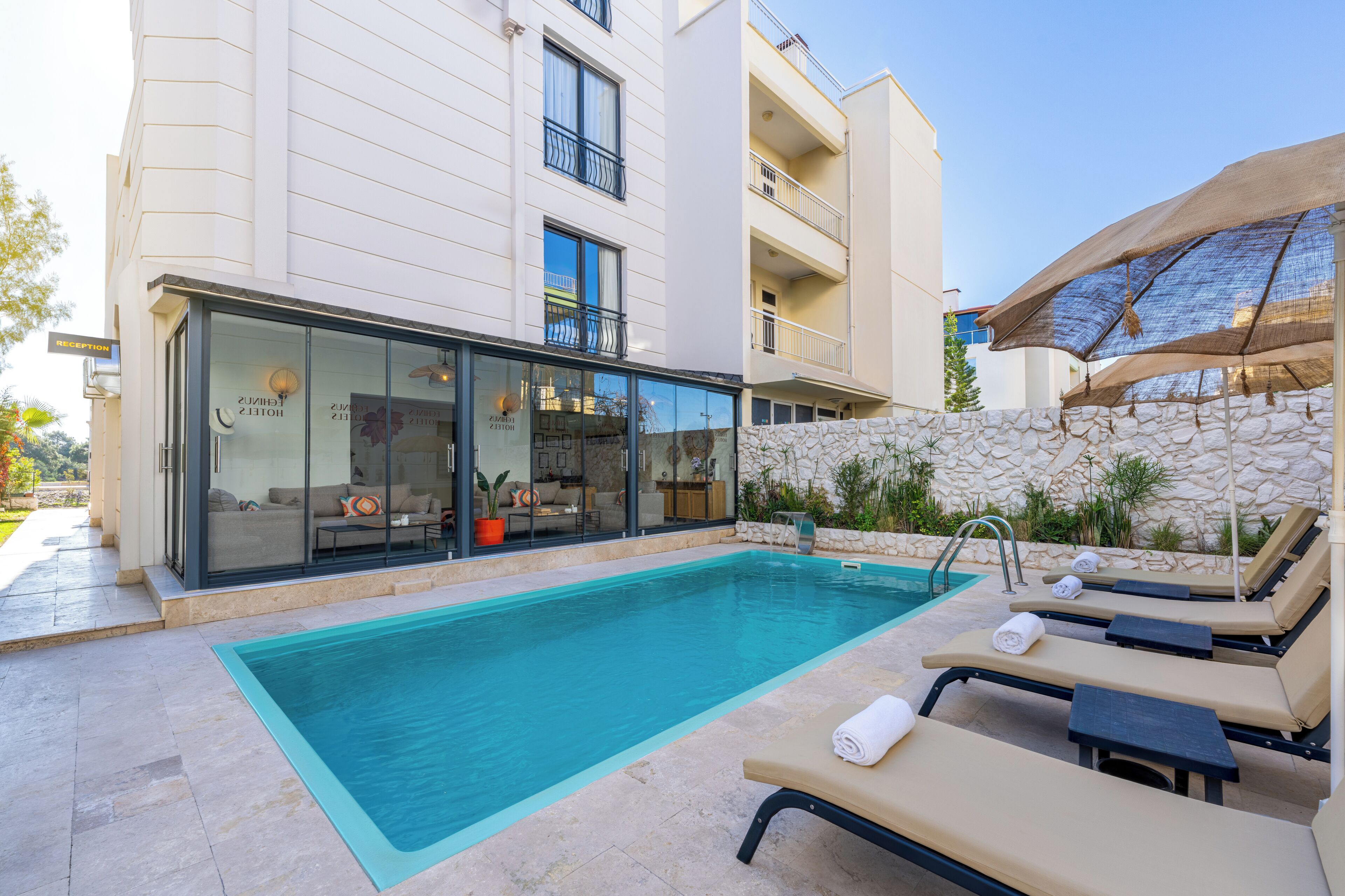 A modern hotel with a swimming pool, sun loungers, and a glass-enclosed lounge area.
