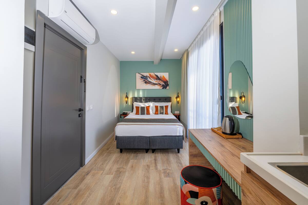 A modern hotel room with a bed, bedside table, lamp, and a view of the hallway.