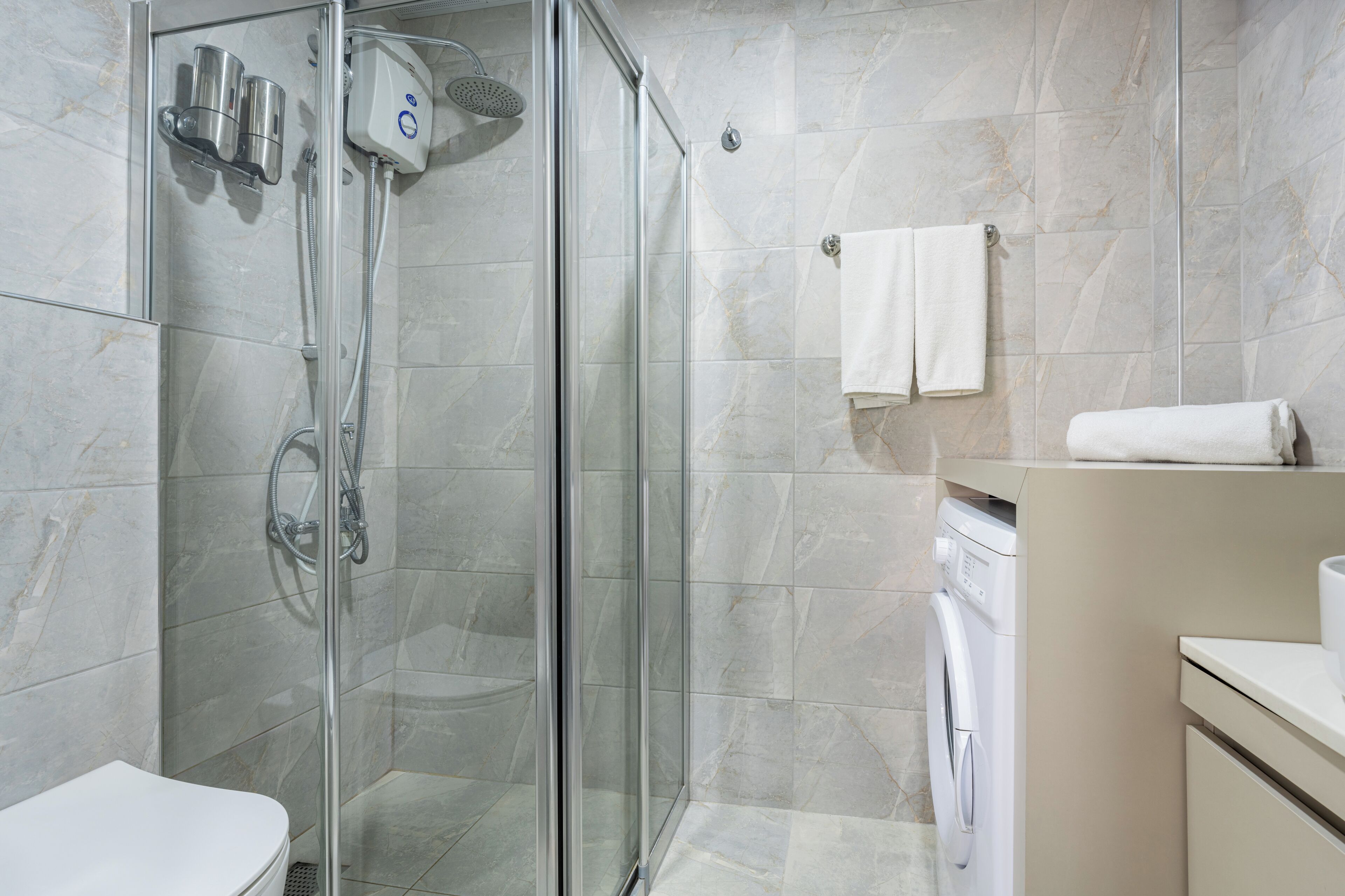 Un baño moderno con cabina de ducha de vidrio, inodoro y lavadora.