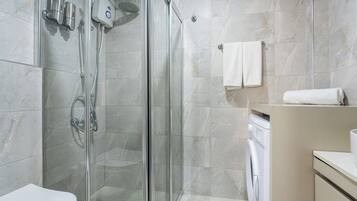 Un baño moderno con cabina de ducha de vidrio, inodoro y lavadora.