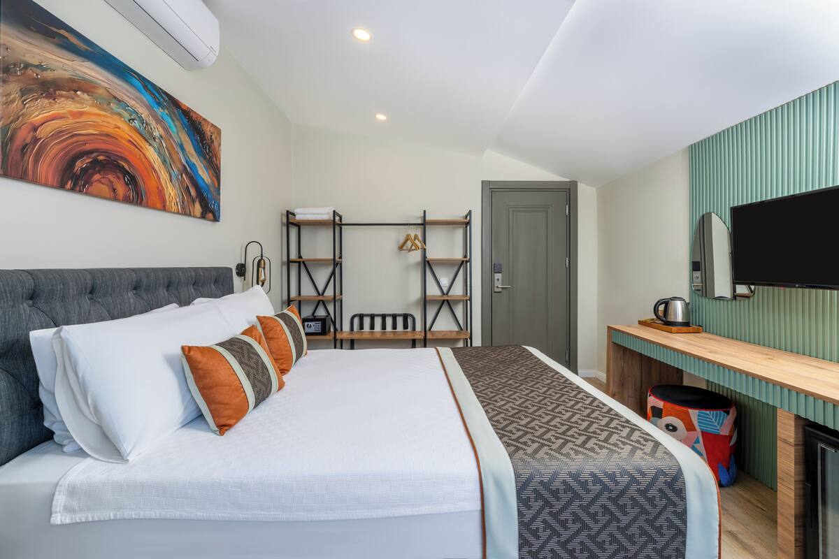 A modern hotel room with a large bed, a desk with a mirror, and a colorful abstract painting on the wall.