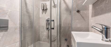 Un baño moderno con ducha envuelta en vidrio, un lavabo blanco con grifo cromado y azulejos de mármol.