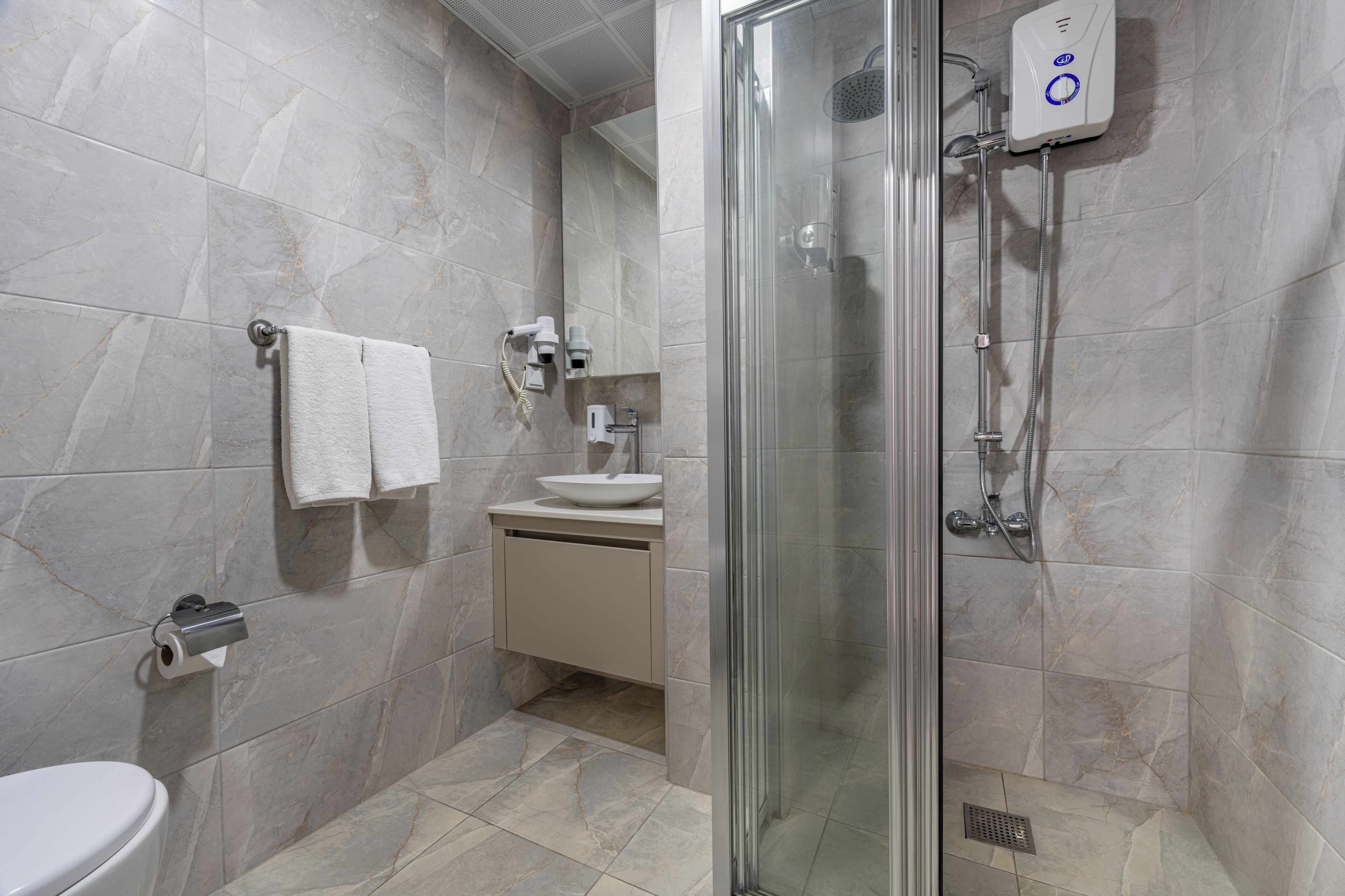 Un baño moderno con ducha de vidrio, inodoro, lavamanos y toallero.