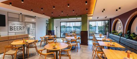 A modern cafe with wooden tables and chairs, a large window with a view, and a wall with a beer-related poster.