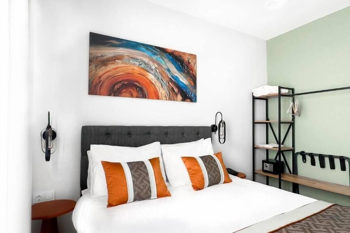 A hotel room with a bed, a painting, a wardrobe, and a nightstand.