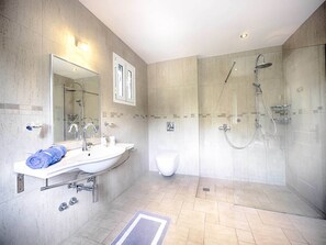 A modern bathroom with a large mirror, two sinks, a shower, and a toilet. - Villa Afionas (Corfu)