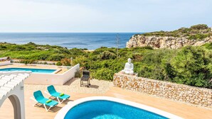 A pool area with lounge chairs, a Buddha statue, and a view of the sea.
