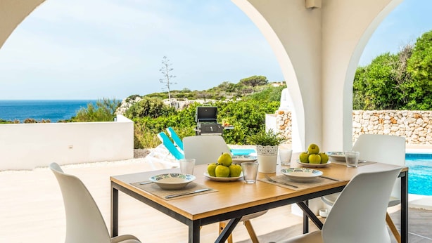 A dining area with a view of the sea, a pool, and a barbecue grill.