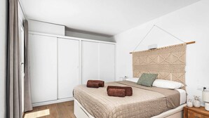 A bedroom with a bed, a wardrobe, a nightstand, and a wall-mounted macrame piece.