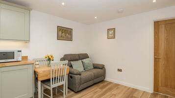 A compact living space with a kitchenette, a dining table with chairs, a grey sofa, and a wooden door.