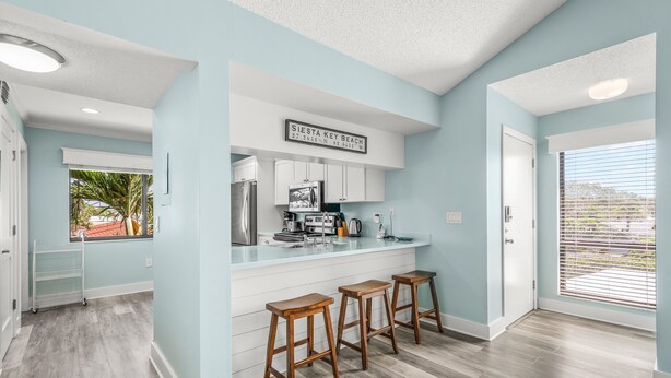 Una cucina moderna con mobili bianchi, un frigorifero in acciaio inossidabile e una zona bar con sgabelli.