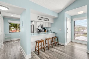 A modern kitchen with white cabinets, a stainless steel refrigerator, and a bar area with stools. - Updated, 2nd Floor Garden unit, Siesta Dunes 7-201 (Sarasota)