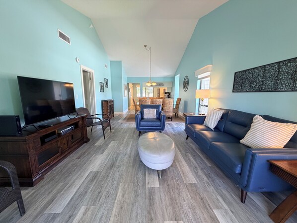 A living room with a TV, sofa, ottoman, and chairs. - Updated, 2nd Floor Garden unit, Siesta Dunes 7-201 (Sarasota)