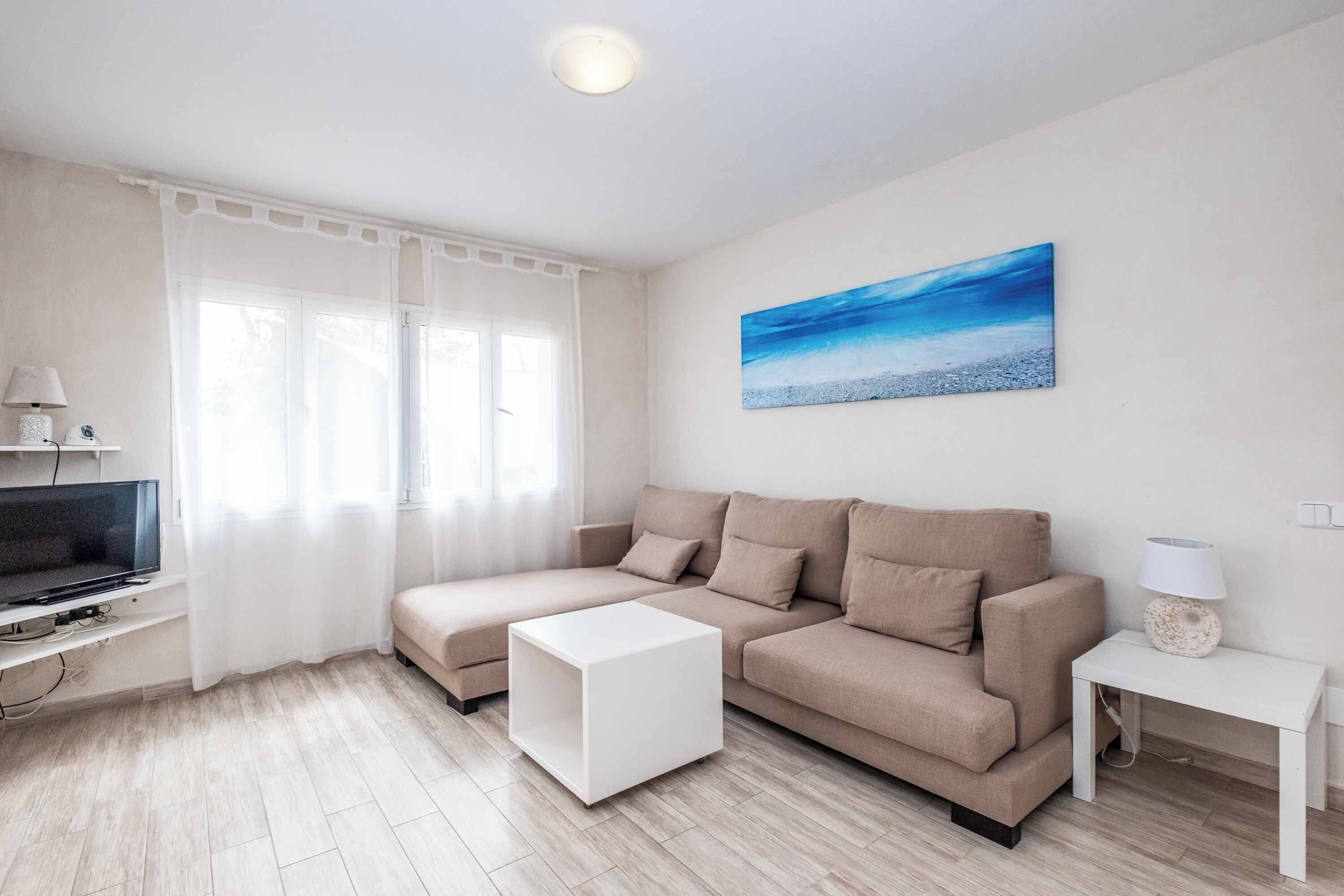 Een moderne woonkamer met een beige bank, een witte salontafel en een flatscreen televisie op een standaard.