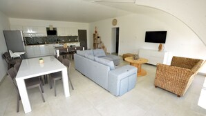 A modern living space with a dining area, a sofa, a TV, and a kitchen in the background. - Gîte Trieves/ Gîte La Passerelle / Gîte Lavars (Lavars)