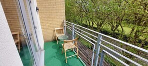 Relax on the balcony with a view of lush greenery, featuring a table and chairs for a peaceful retreat.