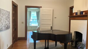Ein Zimmer mit einem Flügel, Holzböden, einer weißen Tür und einem Kamin.