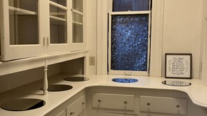 Eine Küche mit weißen Schränken, einem Fenster mit blauer Glasbeschichtung und einem gerahmten Zitat an der Wand.