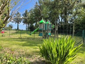 Un parque infantil con tobogán y estructuras para escalar, rodeado de árboles y césped.