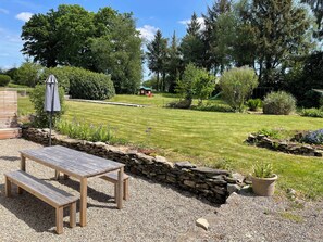 Un jardín con un banco de madera, un muro de piedra y un cobertizo pequeño.