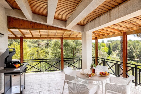 A covered patio with a grill, white wicker furniture, and a table with fruit and drinks. - Platres Forest Panorama (Platres)