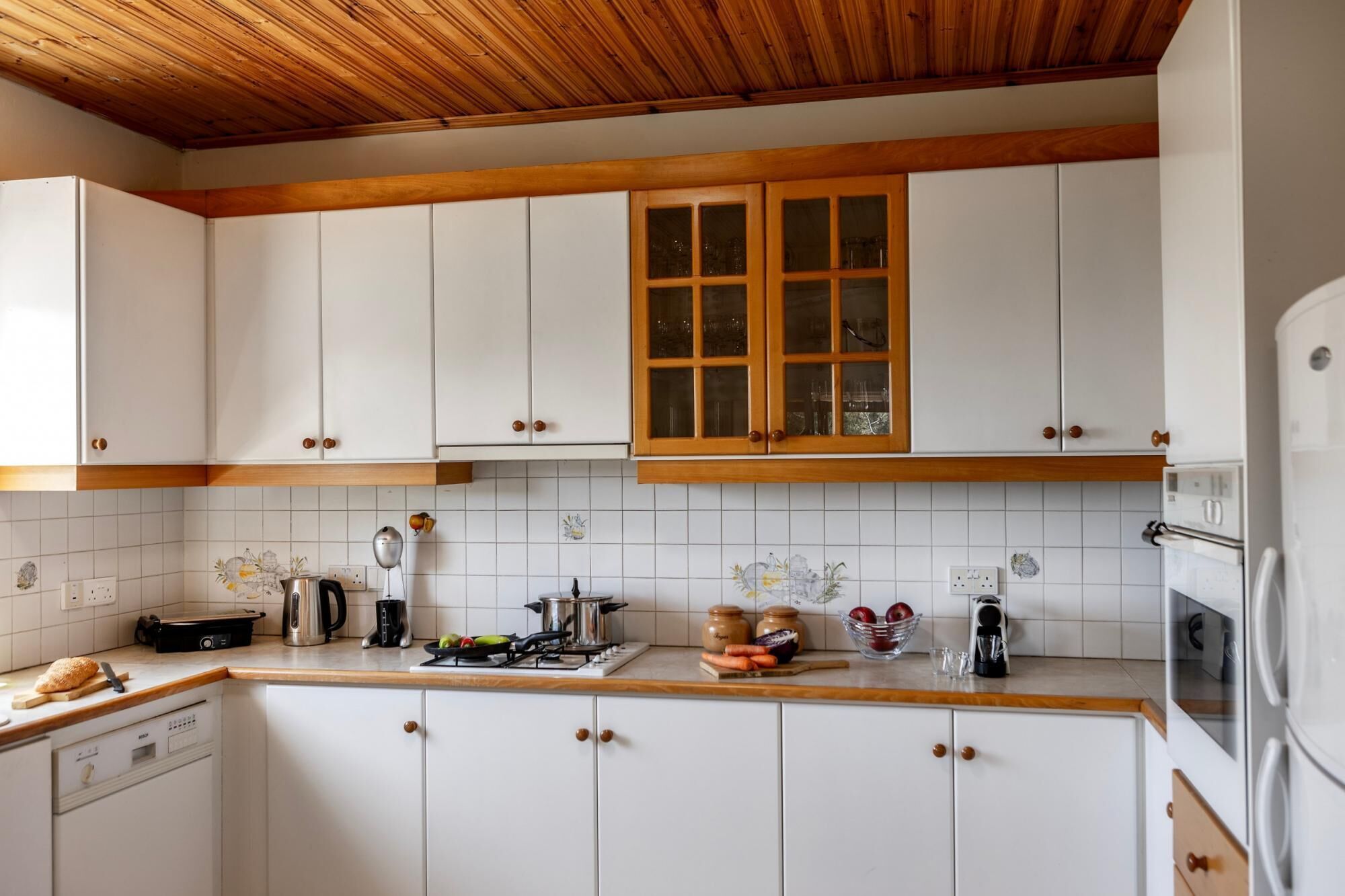 Une cuisine avec des meubles blancs, un plafond en bois et une fenêtre à carreaux.