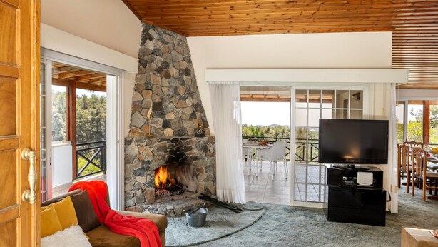 A cozy living room with a stone fireplace, a television, and a comfortable seating area. - Platres Forest Panorama (Platres)
