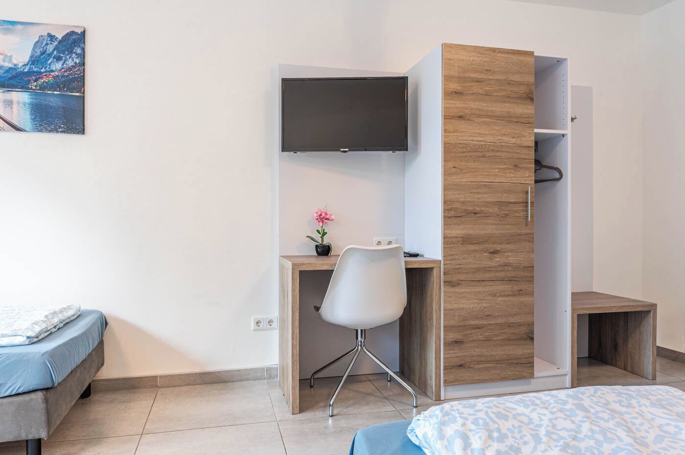 Quarto com cama, escrivaninha com cadeira, televisão e guarda-roupa de madeira.