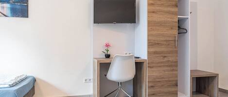 Quarto com cama, escrivaninha com cadeira, televisão e guarda-roupa de madeira.