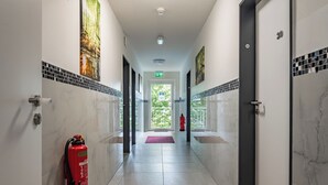 Un pasillo con suelos de mármol, puertas a ambos lados, un extintor de incendios a la izquierda y un felpudo rojo en la entrada.
