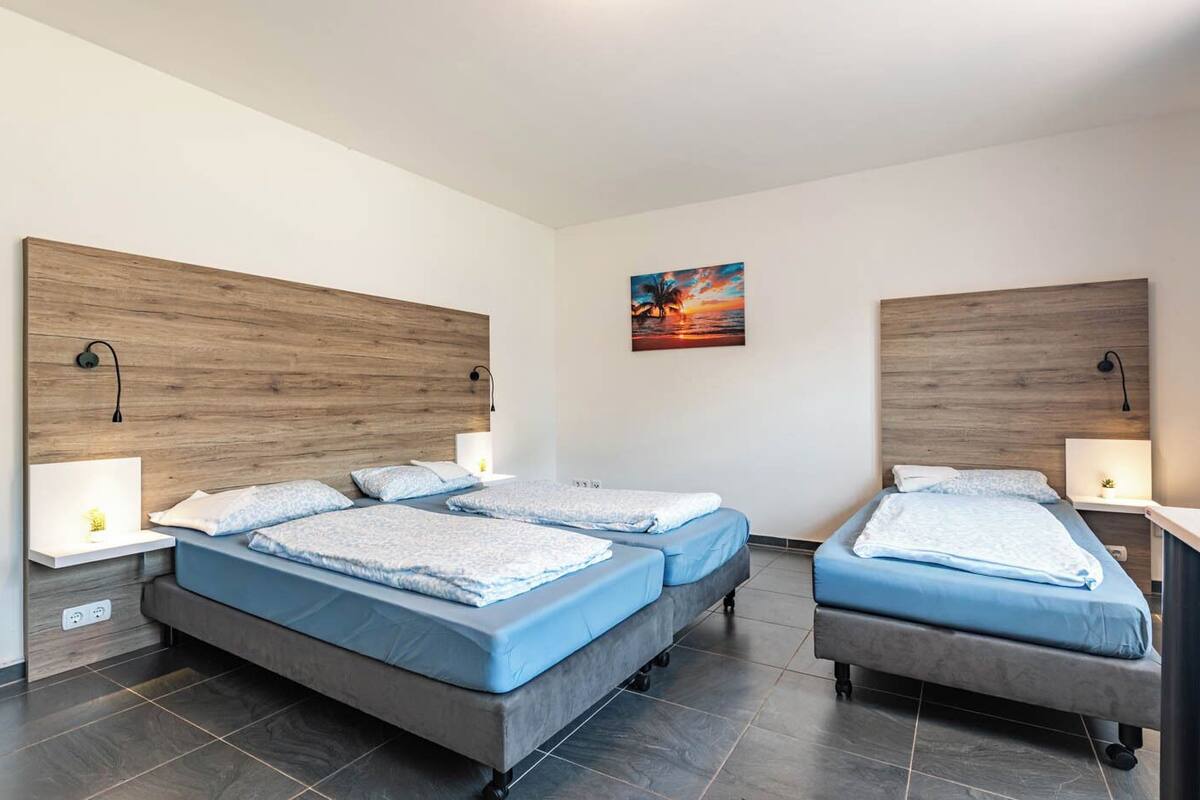 A modern hotel room with two single beds, a wooden headboard, bedside lamps, and a painting on the wall.