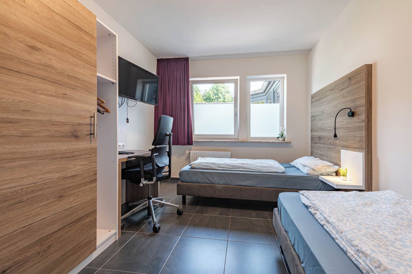 Un dormitorio con escritorio, dos camas, televisor y ventana con cortinas.