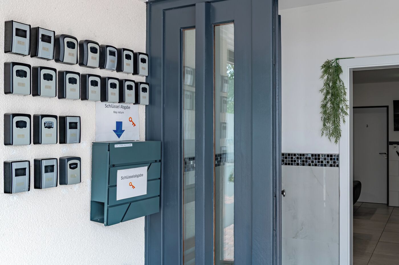 Fila de taquillas con cerradura en una pared, una puerta con panel de vidrio y un pequeño letrero que indica devolución de llaves.