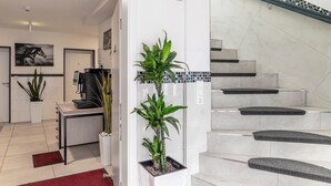 Un vestíbulo de hotel con mostrador de recepción, una escalera y plantas en macetas.