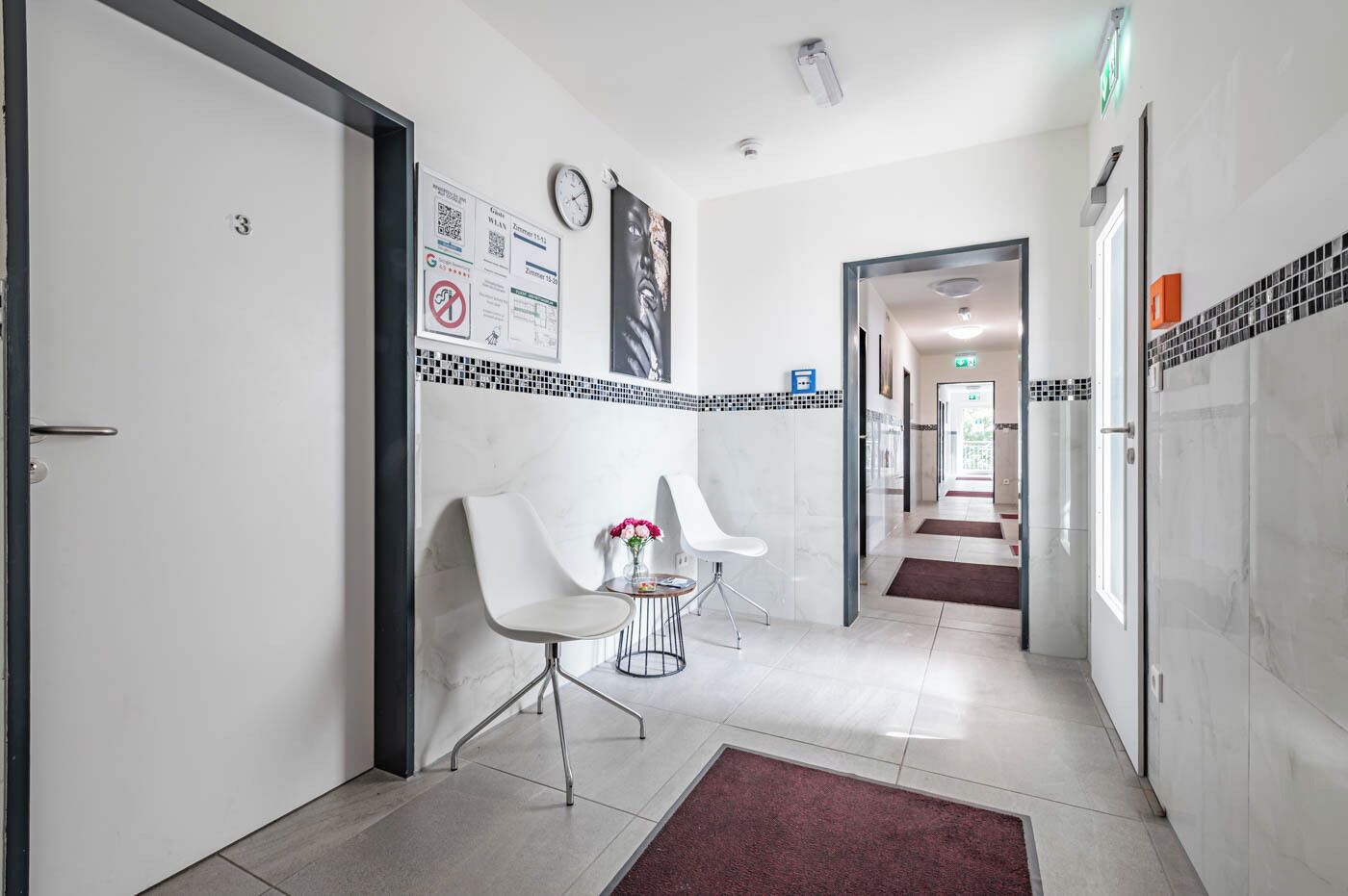 A hotel corridor with a reception desk, a clock, and a sign with QR codes.