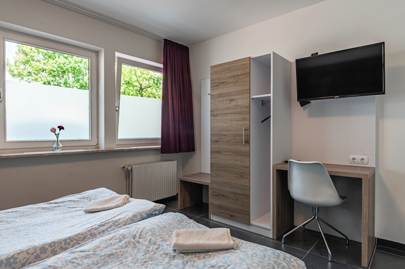Camera d'albergo con due letti, una scrivania, una sedia, un televisore e una finestra vista alberi.