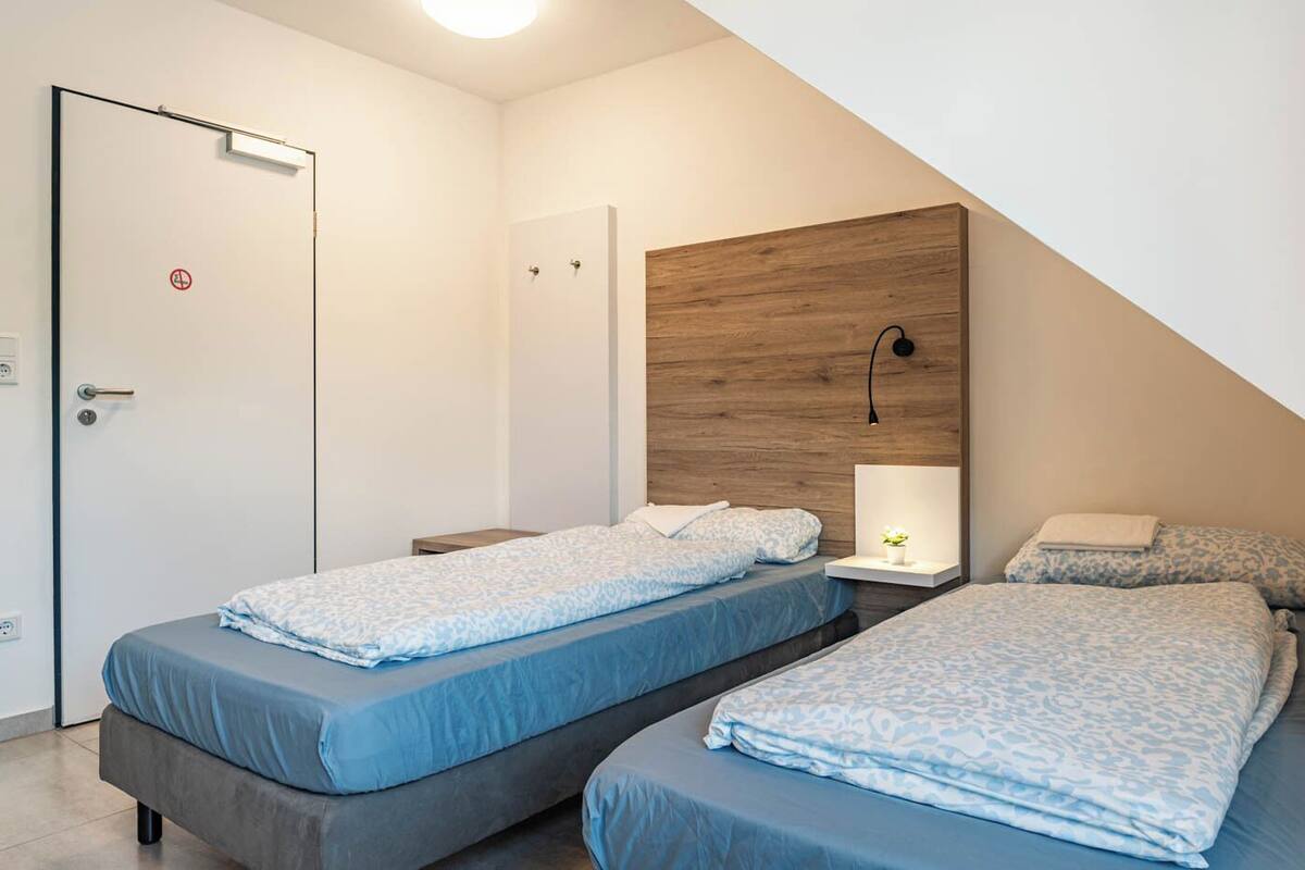 A bedroom with two beds, a wooden headboard, bedside lamps, and a door with a no-smoking sign.