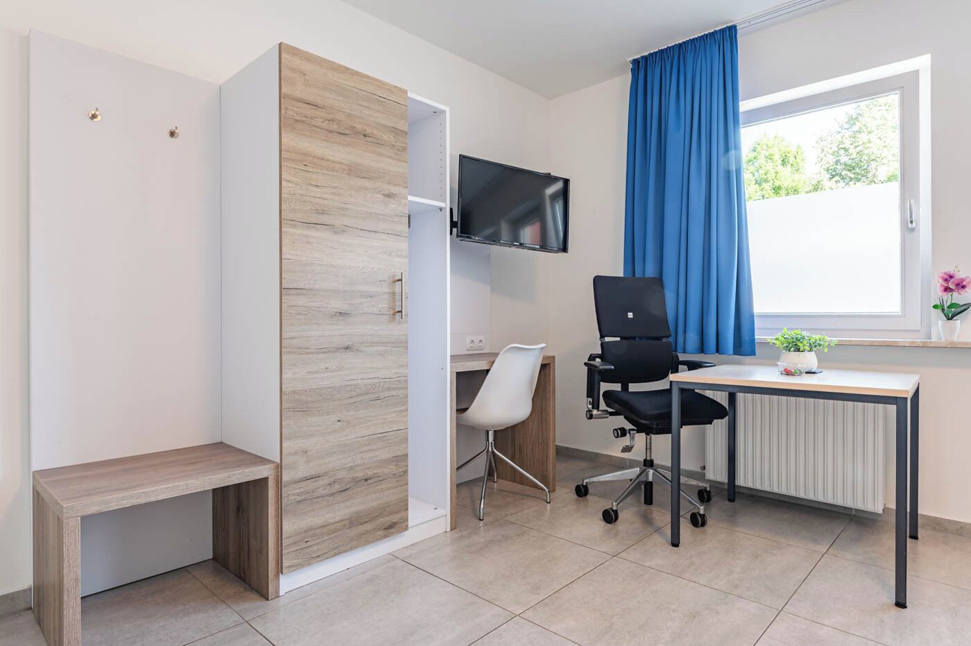 Un espacio de oficina moderno con un armario de madera, un escritorio, una silla, un televisor y una ventana con cortinas.