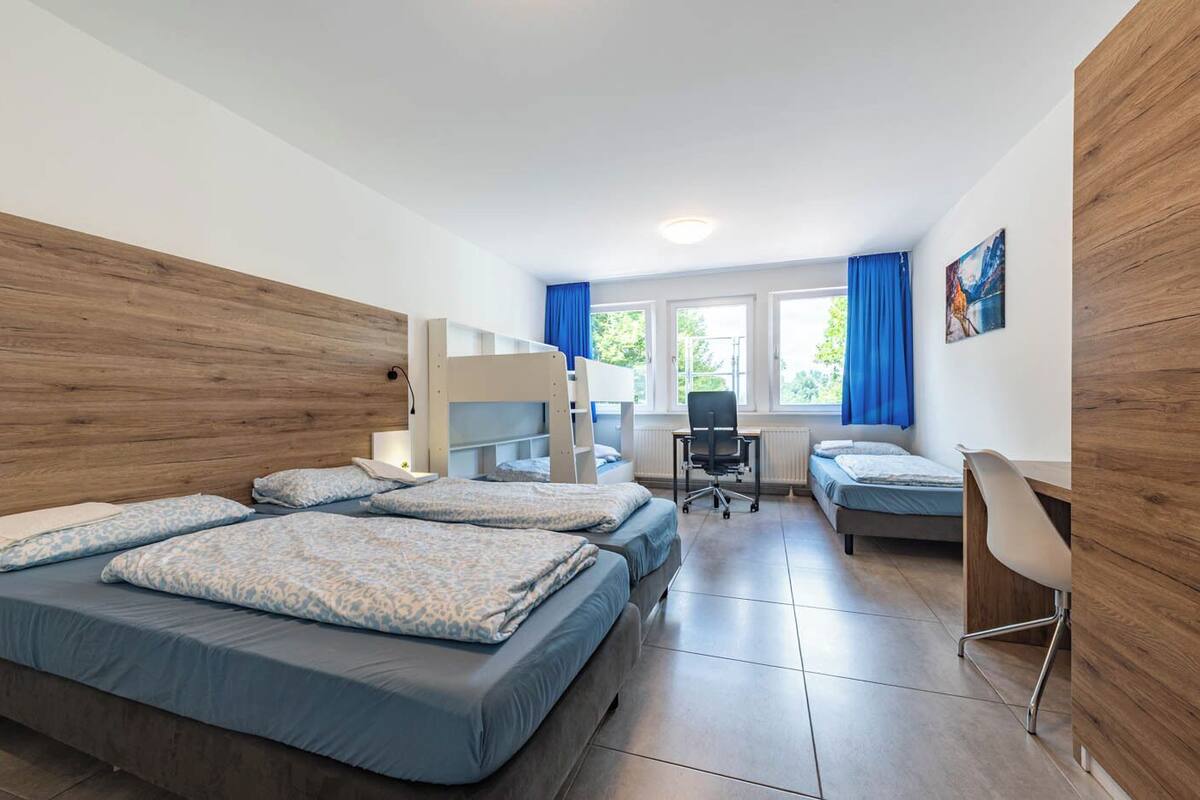 A room with three bunk beds, a desk, and a chair.