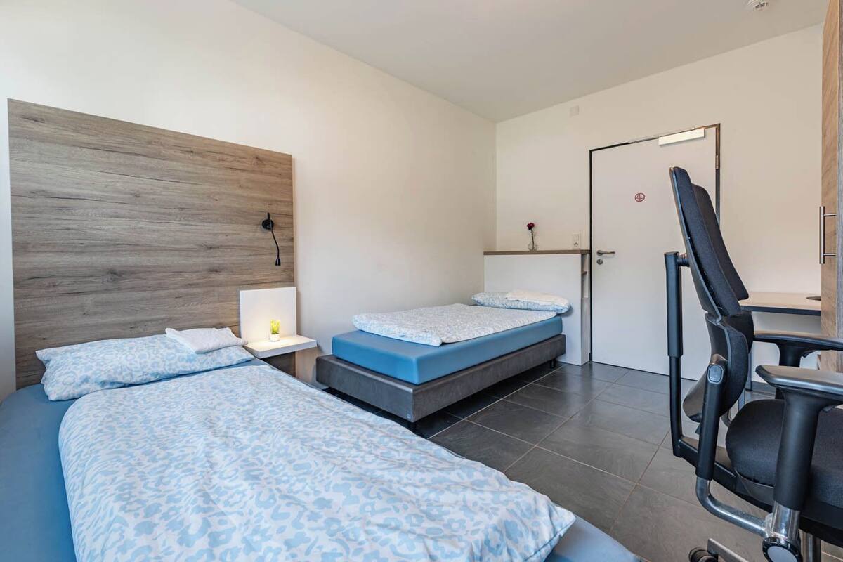 A hotel room with two beds, a desk, and a chair.