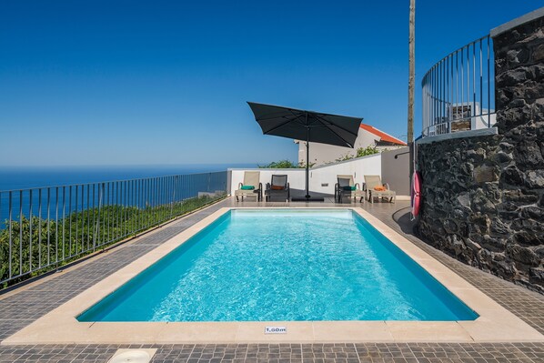 Une piscine rectangulaire à l’eau d’un bleu limpide, entourée d’un mur de pierre et d’une rambarde métallique.