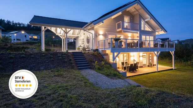 Een twee verdiepingen tellend huis met een overdekte patio en een groot raam met uitzicht op de tuin.